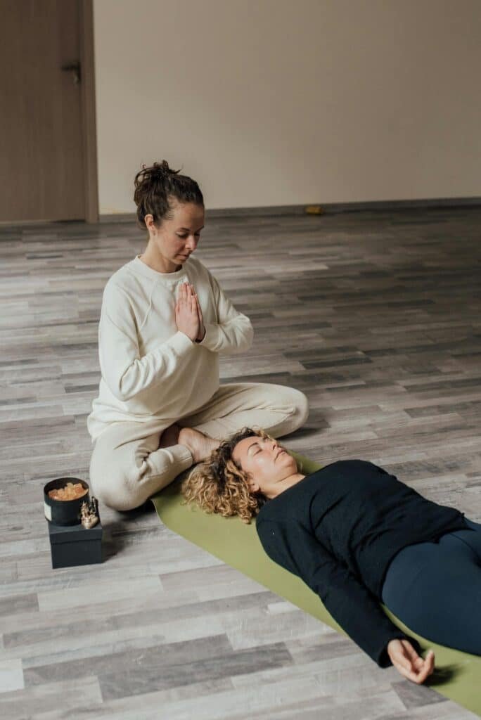 A peaceful indoor meditation session with a guide and a participant on a yoga mat.